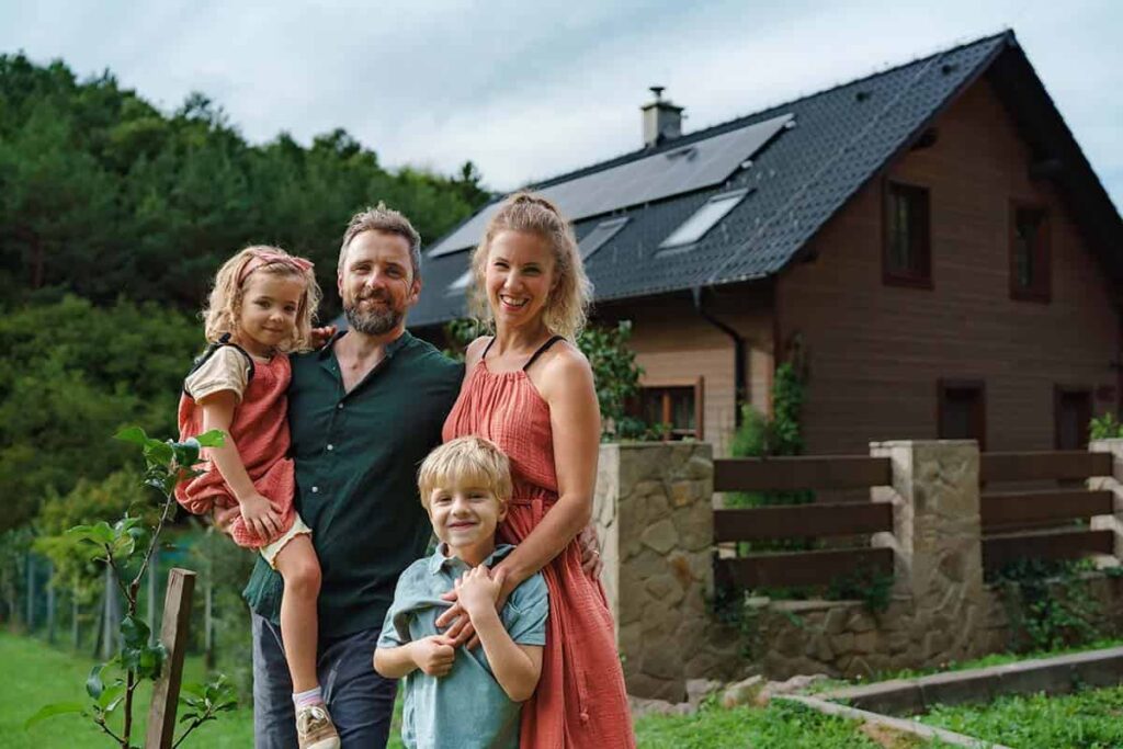 Happy family standing in front of their home. On the roof there are newly installed solar panels