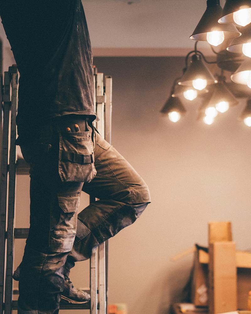 Electrician on a ladder installing a modern chandelier, typical of lighting upgrades in Greenfield, MA.