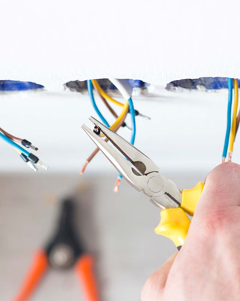 Close-up of an electrician stripping wires for a ceiling fixture, a common service for Greenfield renovations.
