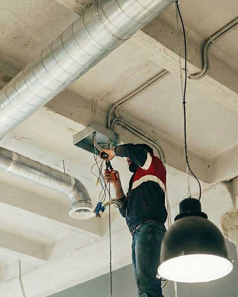 Electrician accessing overhead wiring similar to the electrical preparations needed for commercial solar projects in Greenfield, MA.