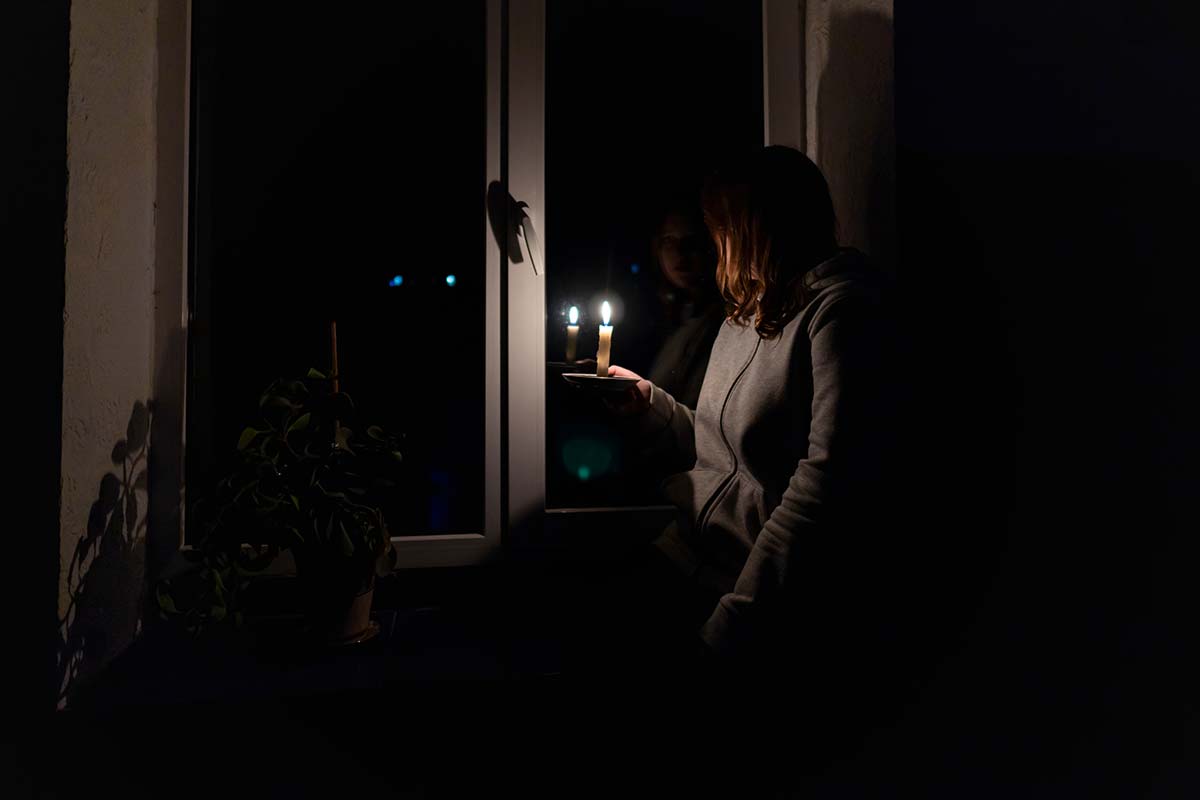 Person using candlelight during a power outage, showing why Greenfield homes may need battery backup with solar.