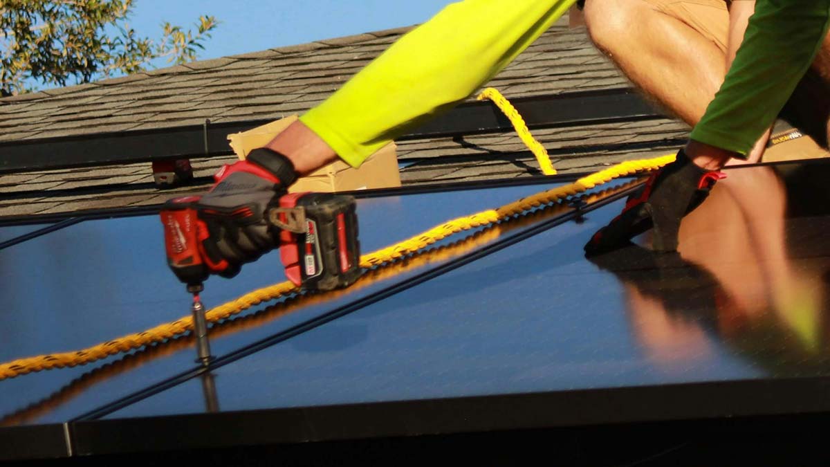 Close-up of a solar installer using a drill to secure panels to a home's roof.