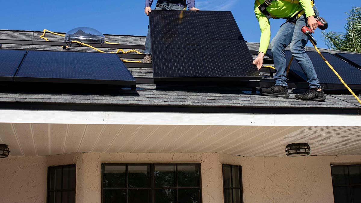 A crew member positions a solar panel during a residential installation on a clear summer day.