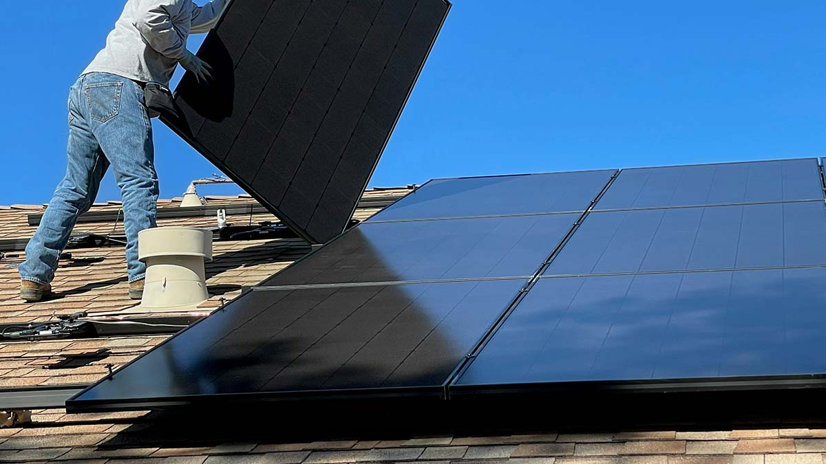 Close-up of a solar installer using a drill to secure panels to a home's roof.